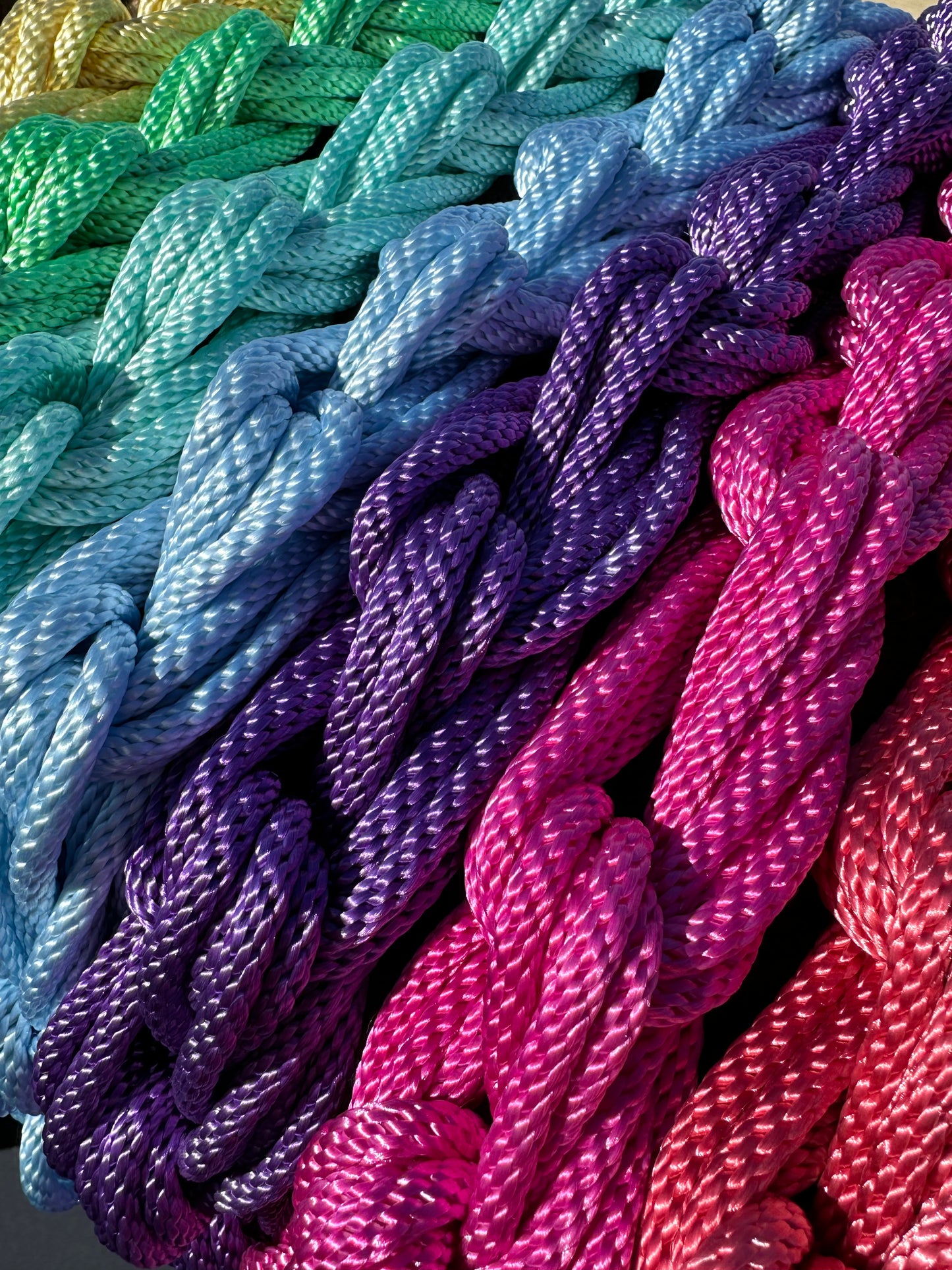 daisy chained nylon rope laid out next to each other to form a rainbow of colors including shades of red, pink, purple, light blue, teal, green, and yellow.